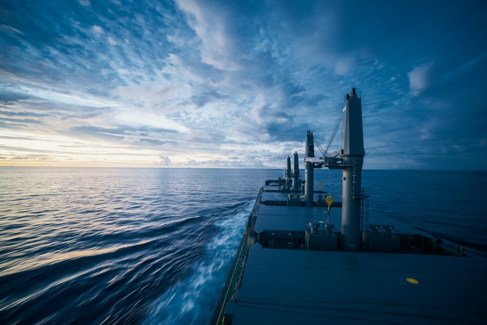 A ship underway at sea, seen along the hull towards the horizon.