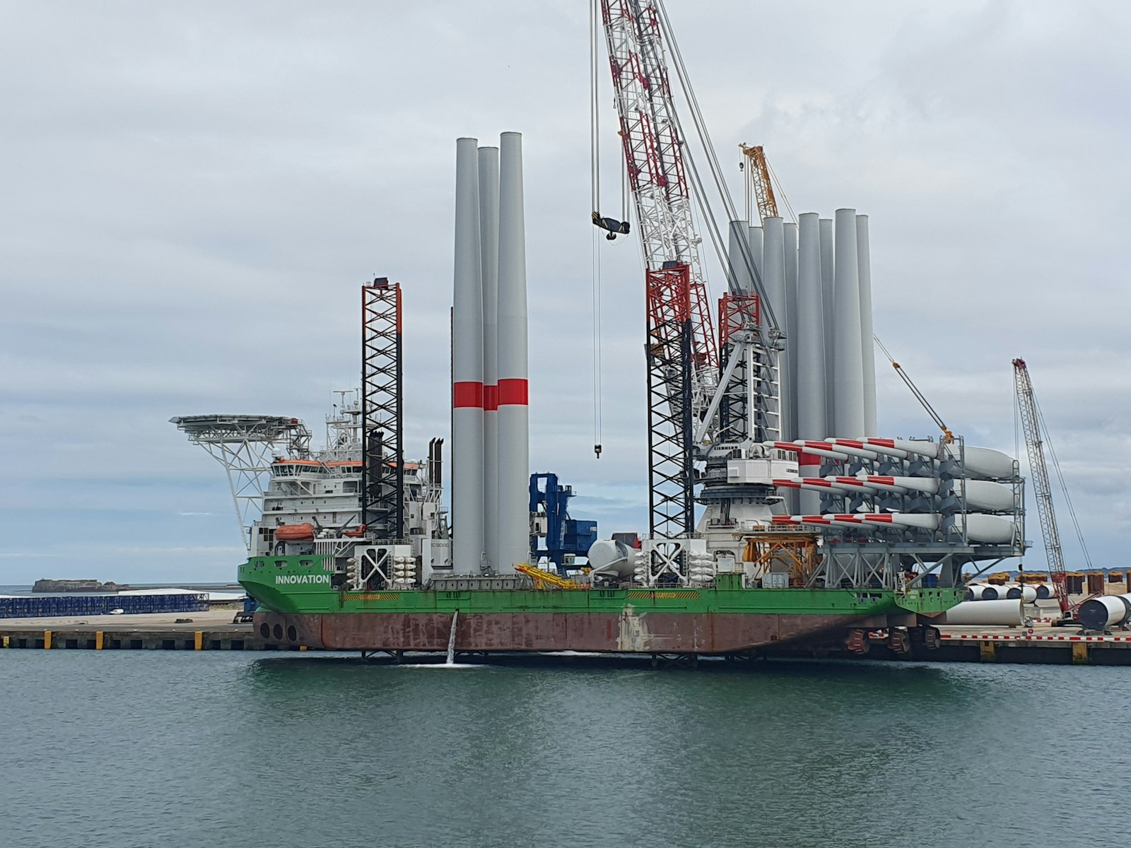 Offshore wind installation vessel loaded with monopiles and tower sections at the quay.